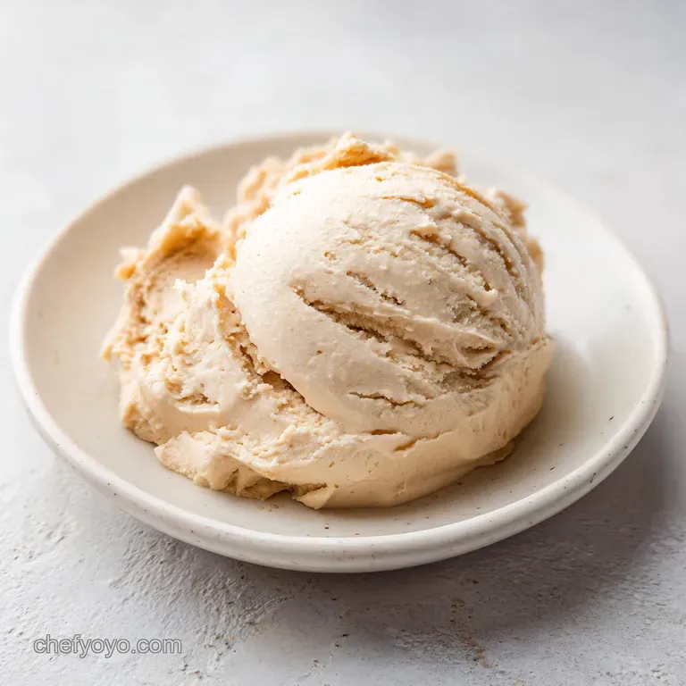 A smooth scoop of pale, buttery dough topped with dark chocolate morsels on a polished white marble surface.