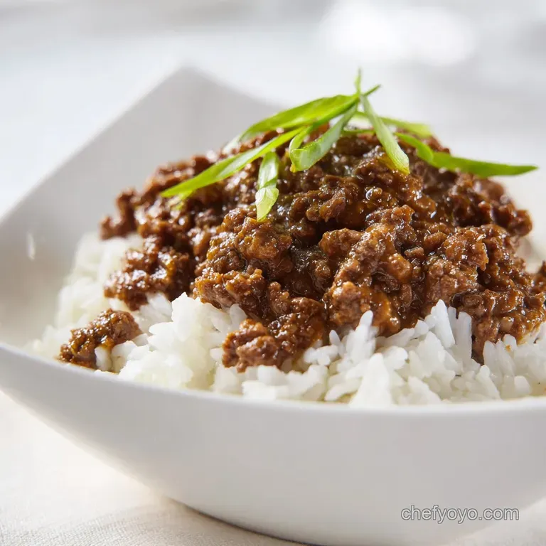 Glazed minced beef over a bed of steaming white rice in a dark bowl, finished with sesame seeds and green onions.