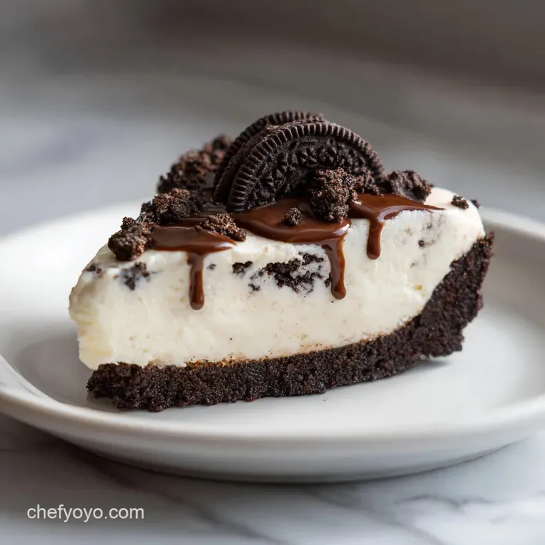 A slice of smooth white cream pie on a white ceramic plate, accented by dark cookie crumbs and a mint leaf.